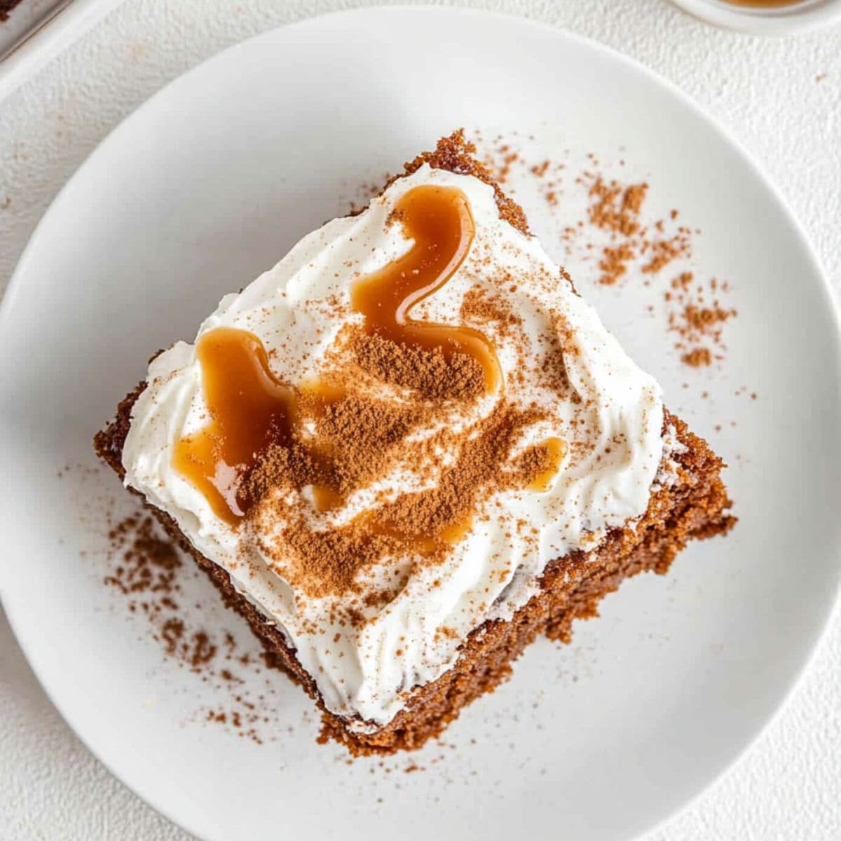 Square slice of gingerbread poke cake with whipped cream on top dusted with crushed gingerbread cookies drizzled with caramel syrup. 