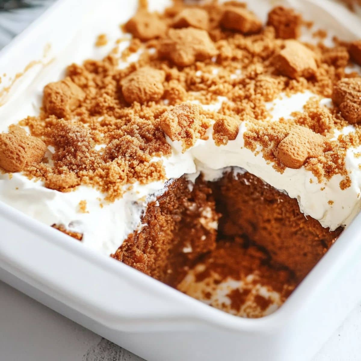 Gingerbread poke cake in a rectangular white baking dish topped with crushed gingerbread cookies on top.