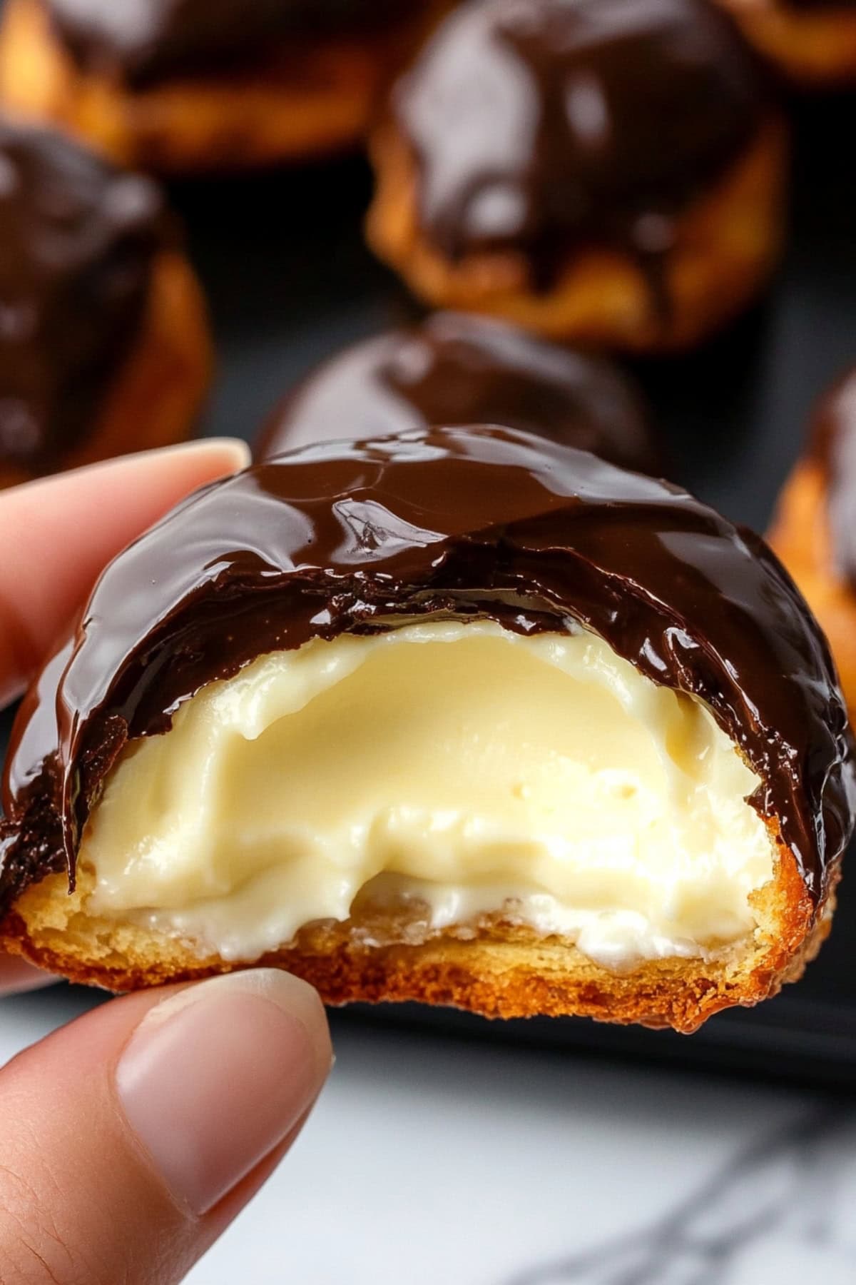 Hand Holding a Profiterole with A Bite Removed