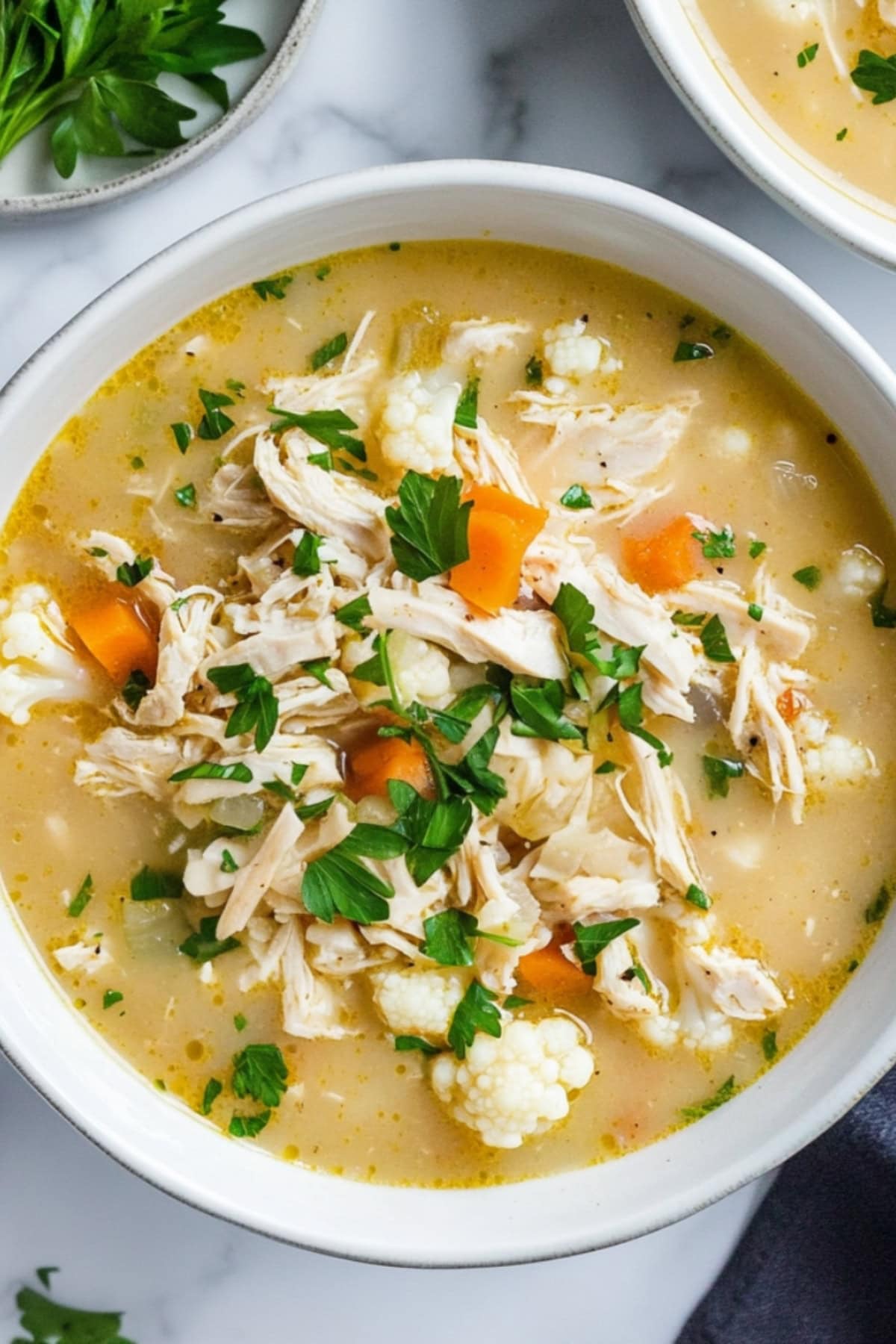 Creamy soup with shredded chicken, cauliflower, carrots, and celery in a bowl.