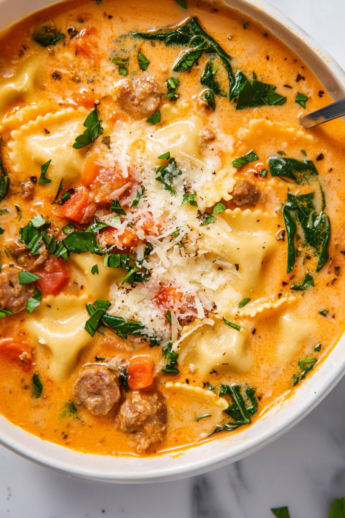 Savory, loaded and creamy ravioli soup with sausage, tomatoes, carrots and spinach in a bowl.