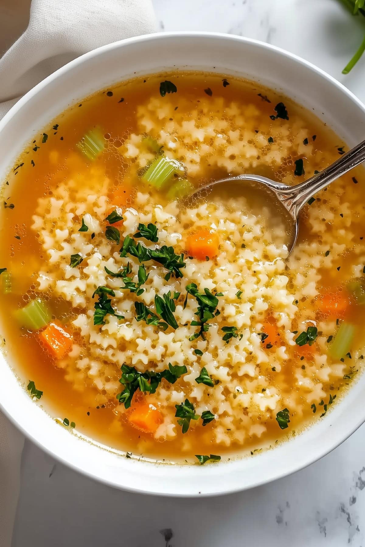 A warm bowl of pastina soup with tiny pasta shapes in a light, clear broth, garnished with fresh parsley.