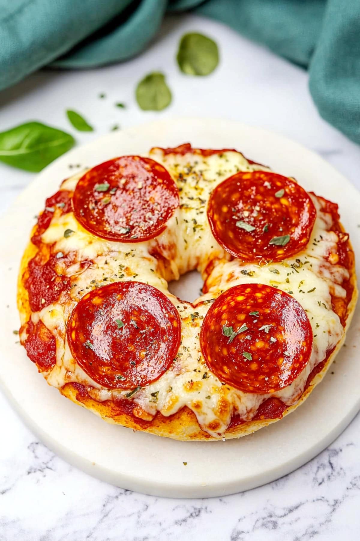 Close-up of a toasted pizza bagel topped with melted cheese, pepperoni, and a sprinkle of herbs.