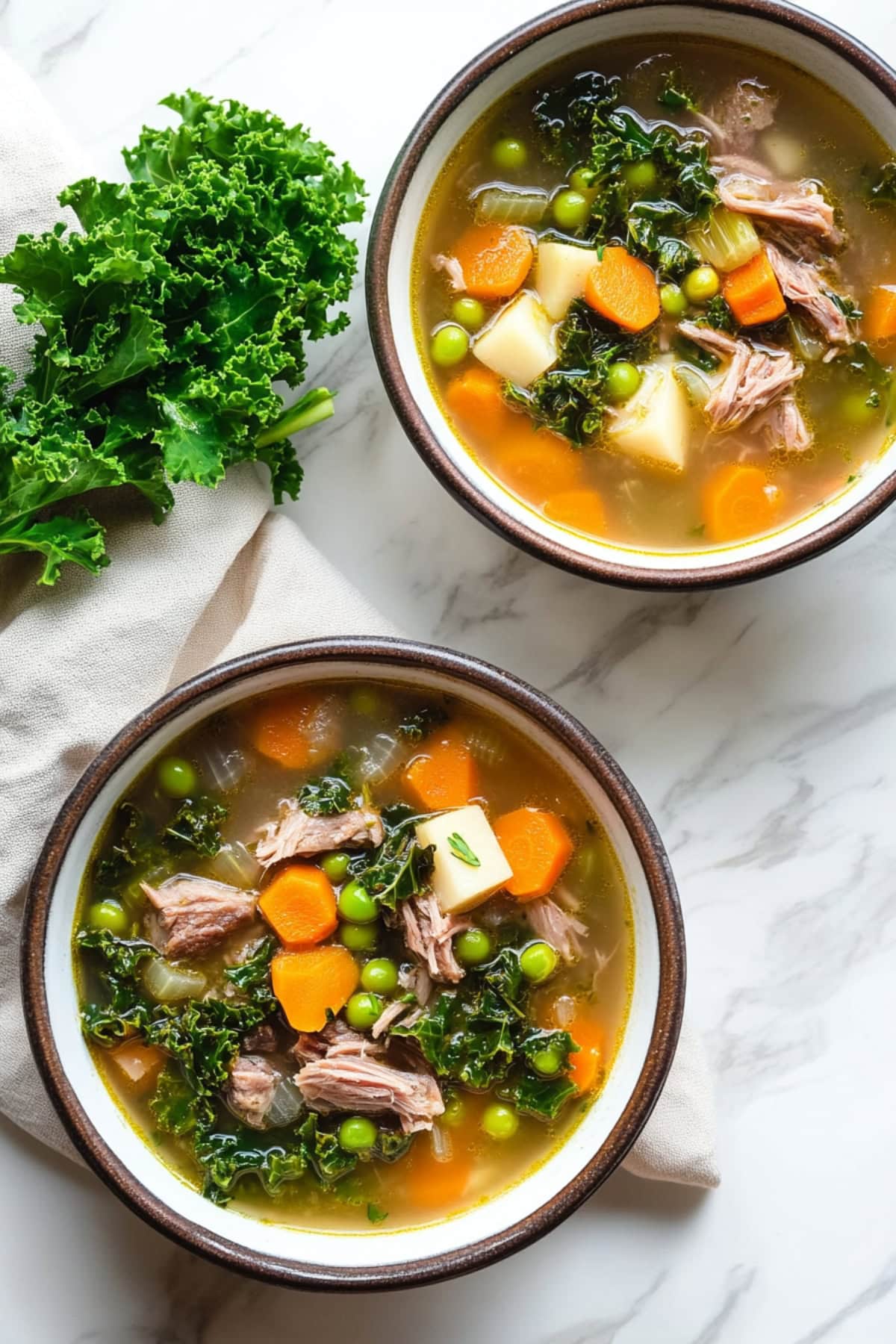 Two bowls of scotch broth with shredded lamb and veggies, top down view.