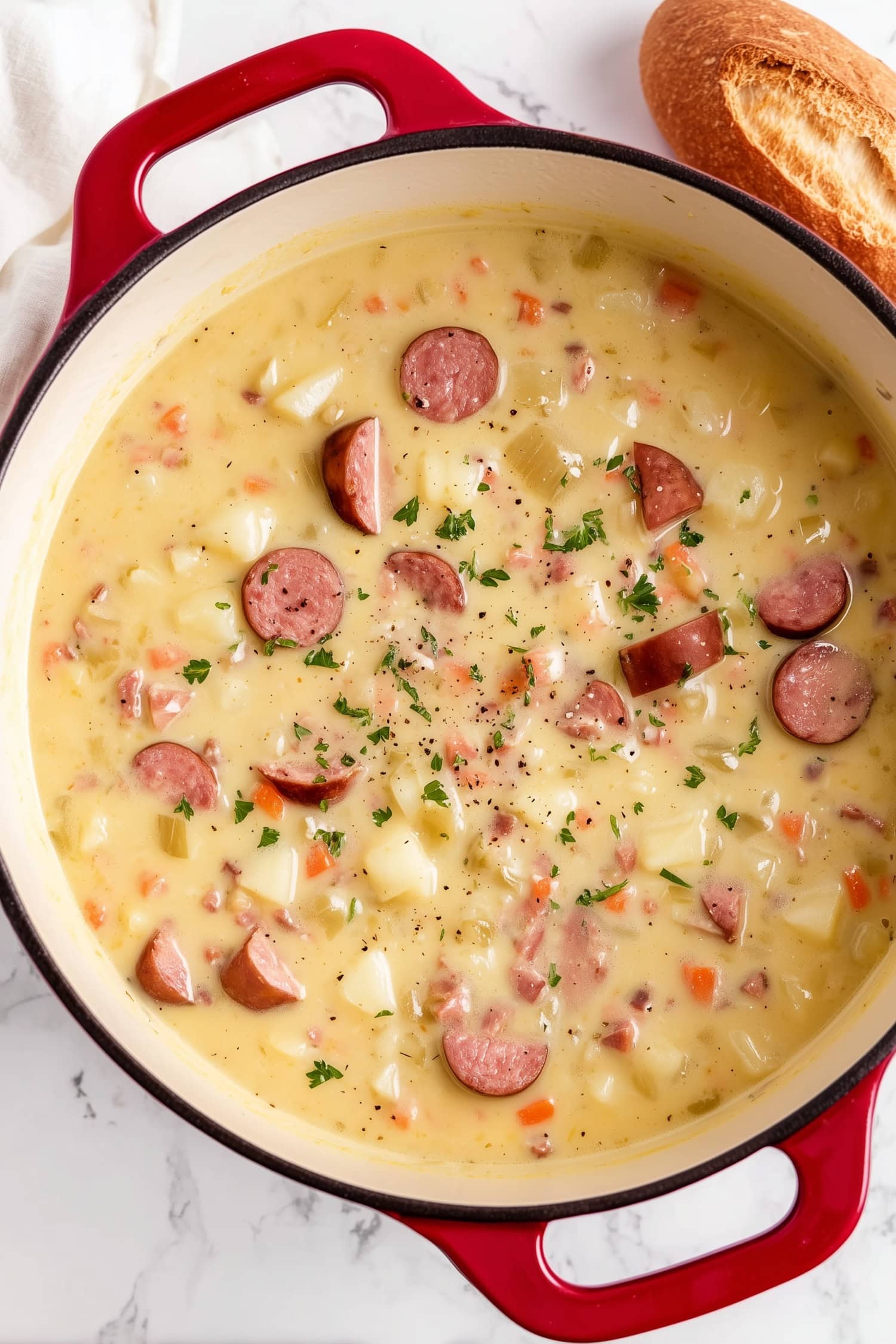 An overhead view of Kielbasa potato soup with onions, celery and carrots with bread on the side.