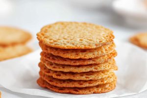 Stack of crispy thin lace cookies stacked on top of a white plate.