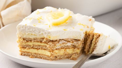 Serving slice of lemon icebox cake in a white plate, fork on the side.