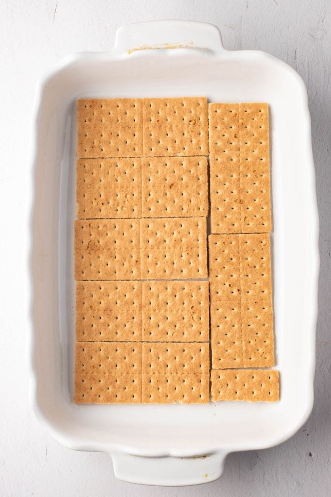 Graham crackers aligned at the bottom of rectangular white baking dish.