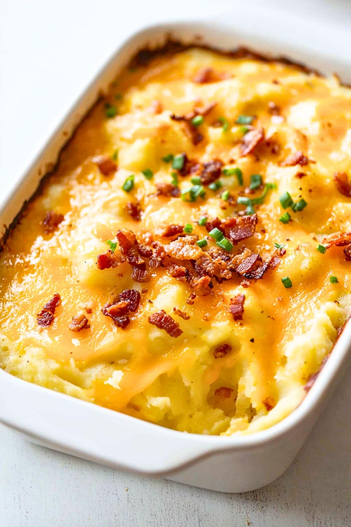 Mashed potatoes with crumbled bacon and melted cheddar cheese in a casserole dish.