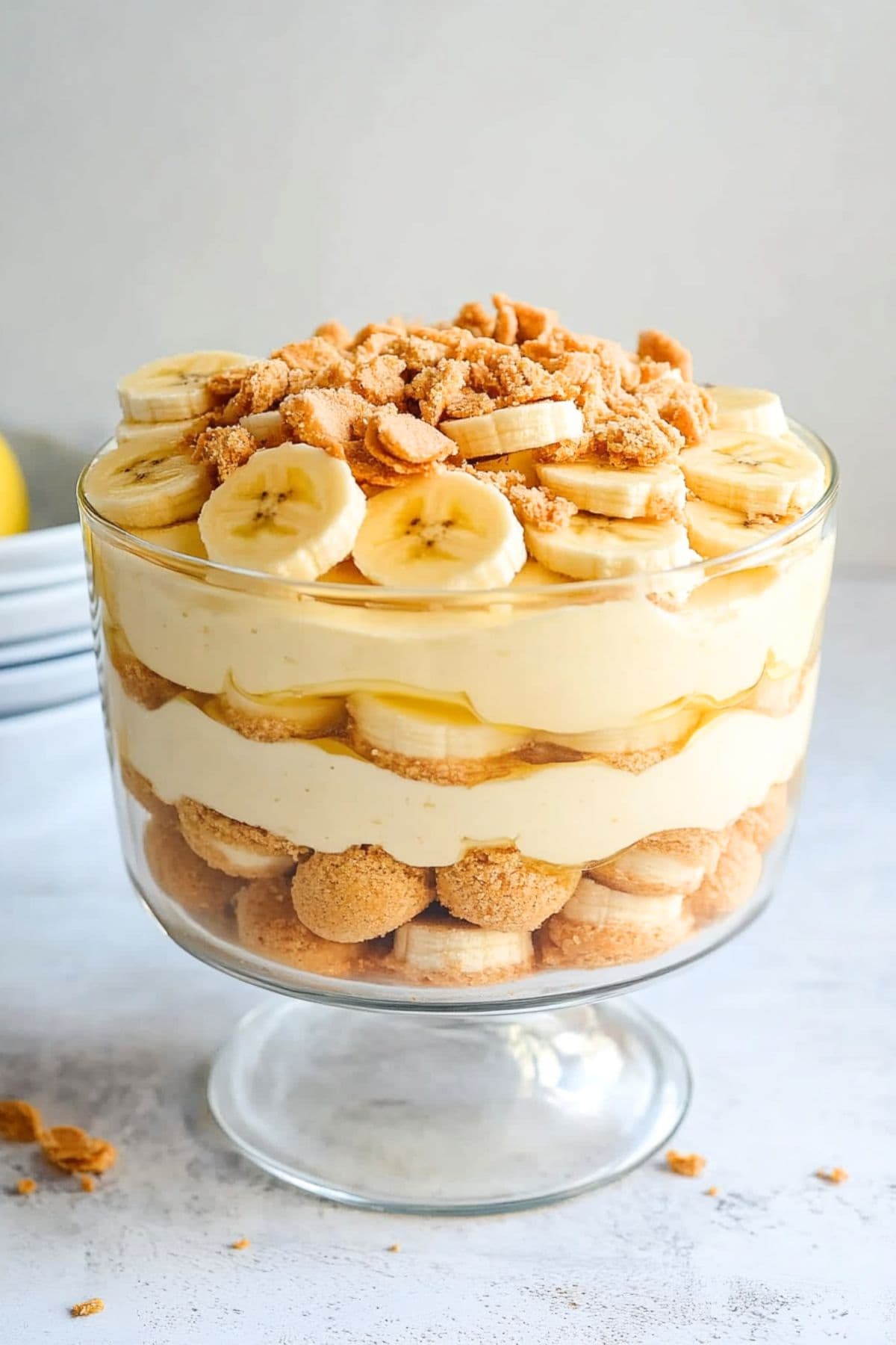 Trifle glass with banana pudding layer sitting on a white concrete table.