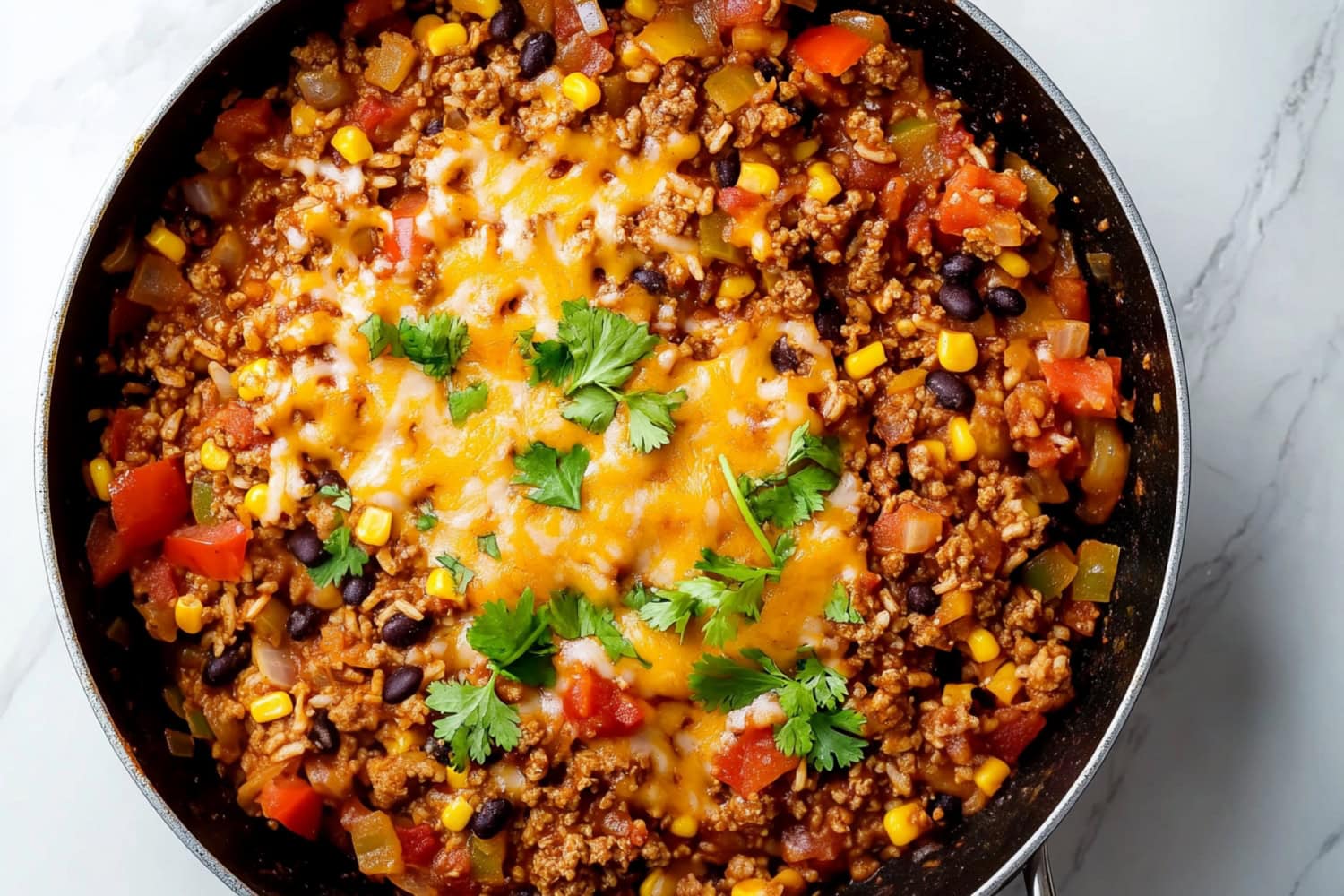 An overhead view of Mexican beef and rice skillet with melted cheese, tomatoes, corn and black beans.