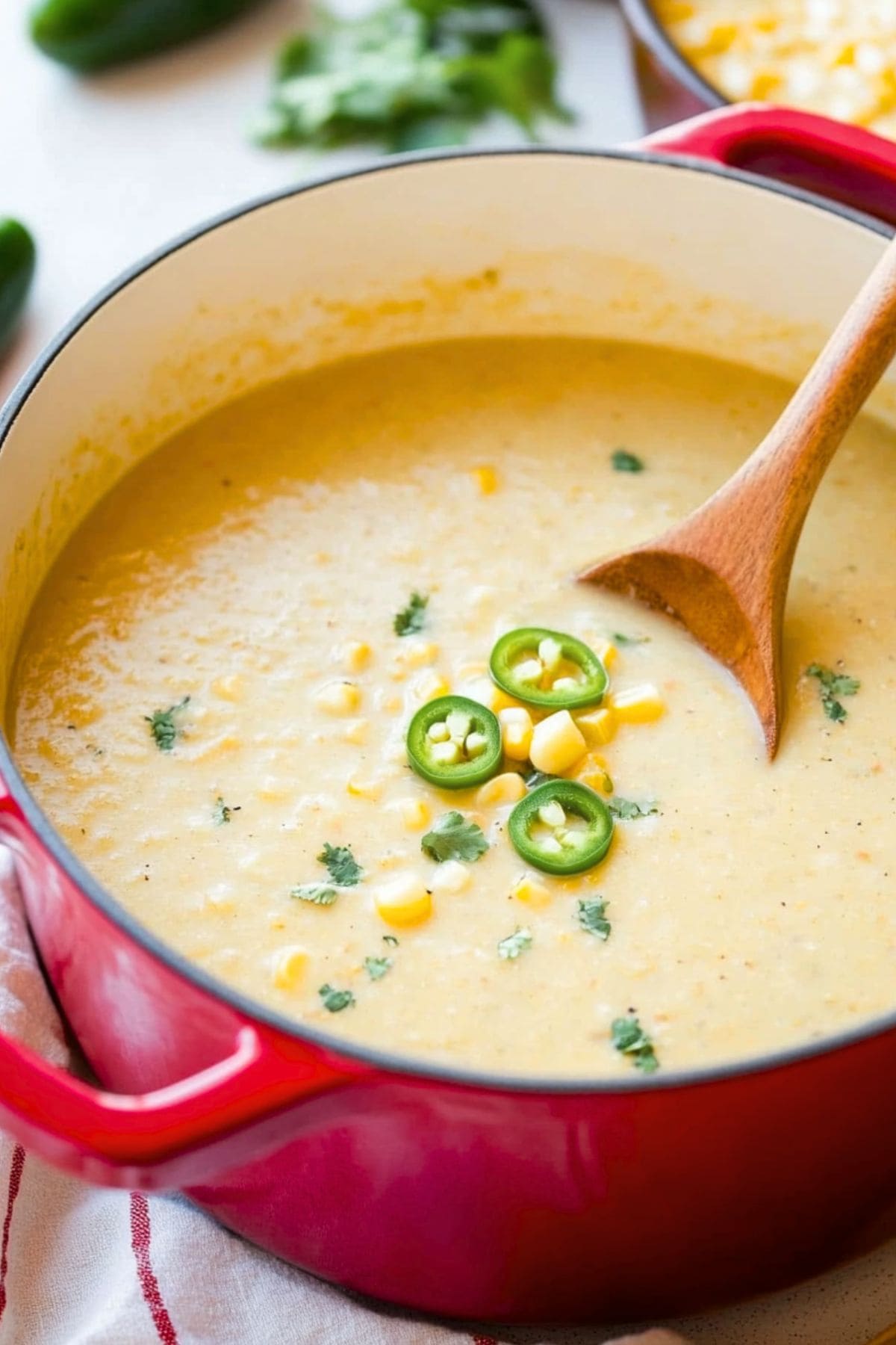 Mexican street corn soup in a red pot, wooden spoon dipped in it.