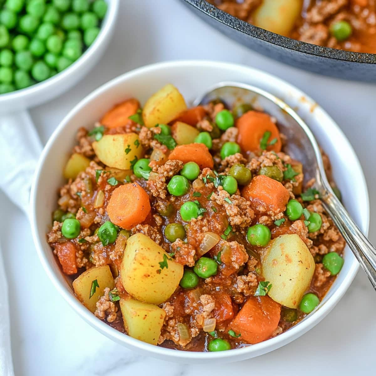 Mexican picadillo with ground beef, carrots, potatoes and  green peas served in a white bowl. 