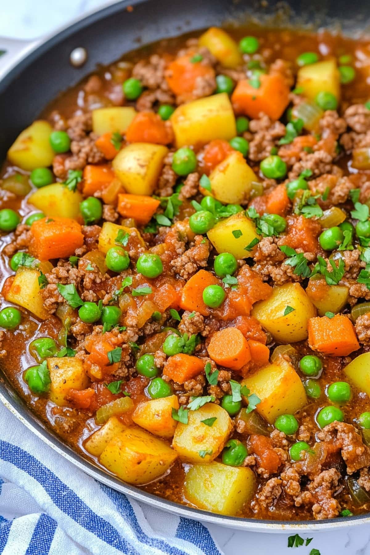 
Ground beef with potatoes, carrots and green peas cooked in a pan.