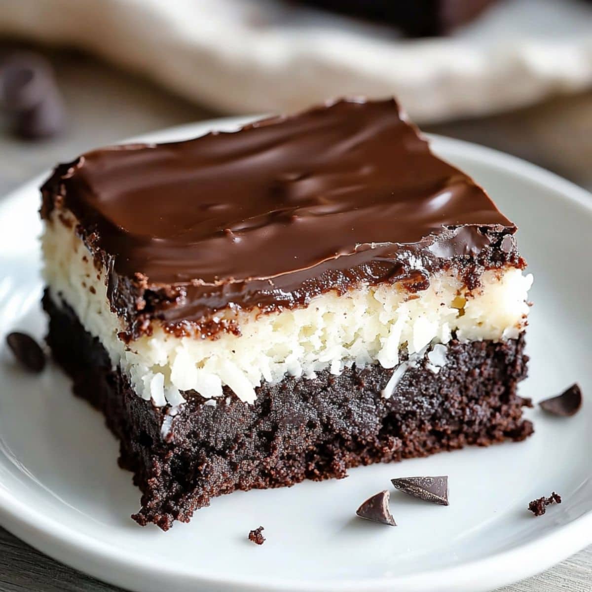 Mounds brownie slice with creamy coconut filling and chocolate ganache served on a white plate.