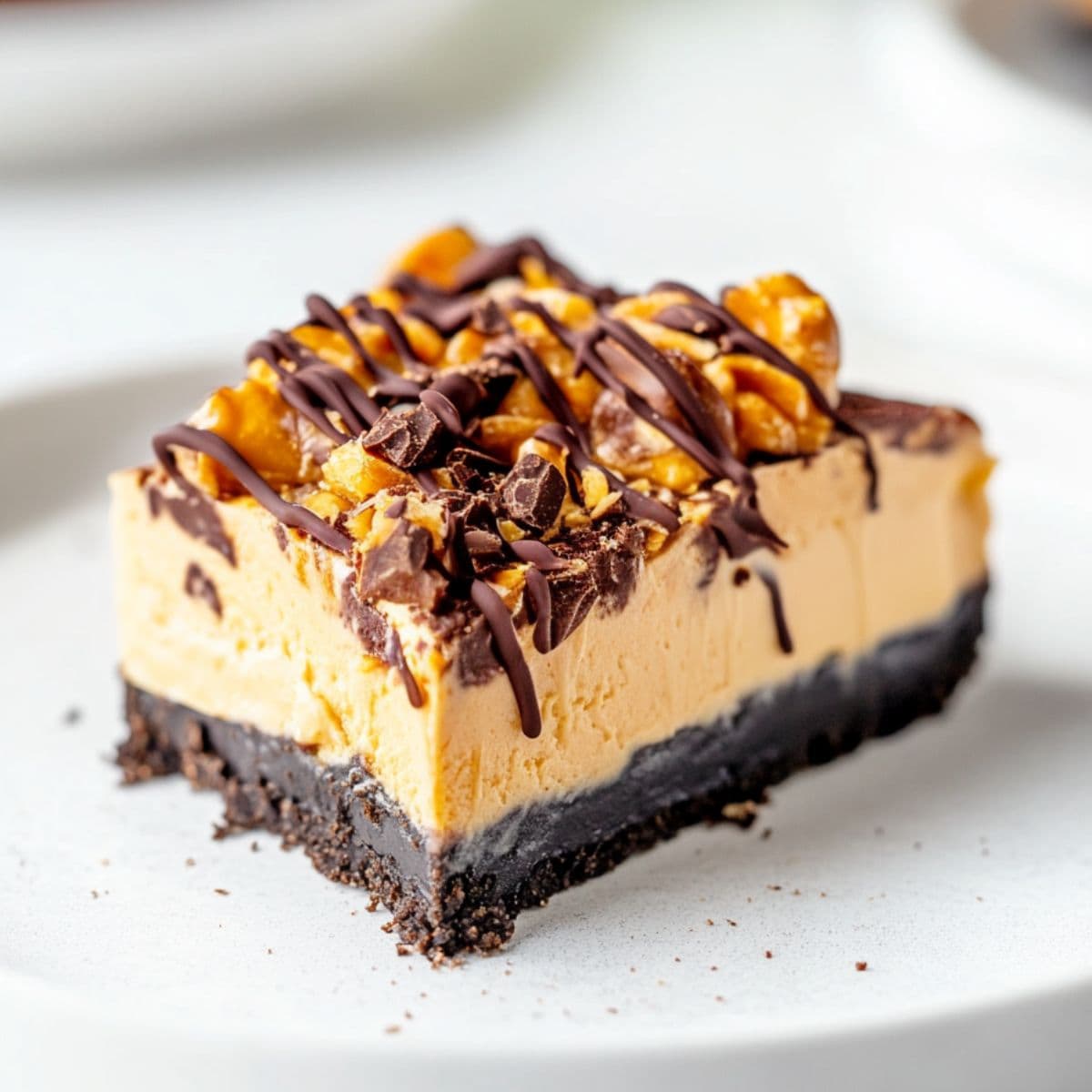 A slice of creamy Butterfinger pie with chopped chocolate drizzled with chocolate on top.