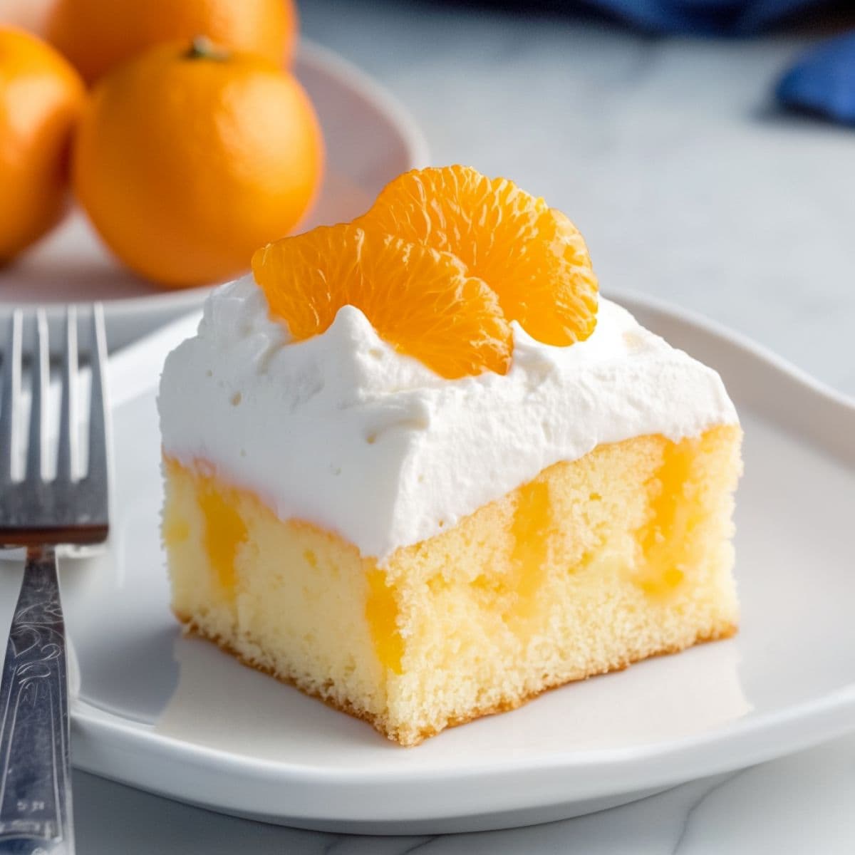 A square slice of orange poke cake with layer of whipped cream on top garnished with orange served in a white plate.