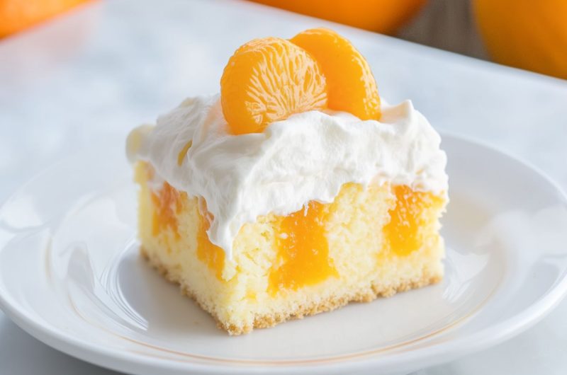 Square slice pf orange poke cake with orange meat garnish and a layer of whipped cream on top served in a white plate.