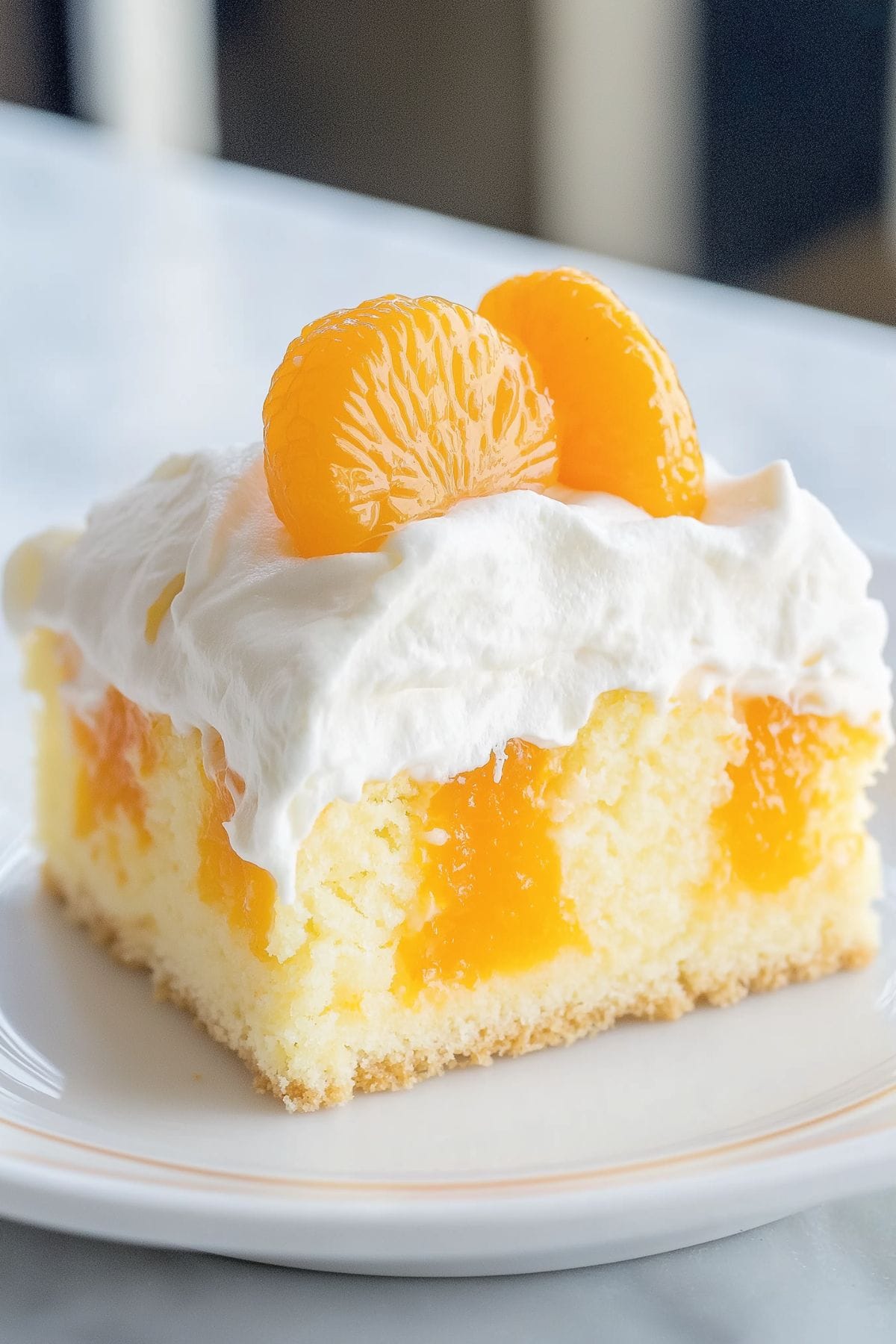 A slice of orange poke cake with whipped cream topping garnished with oranges.