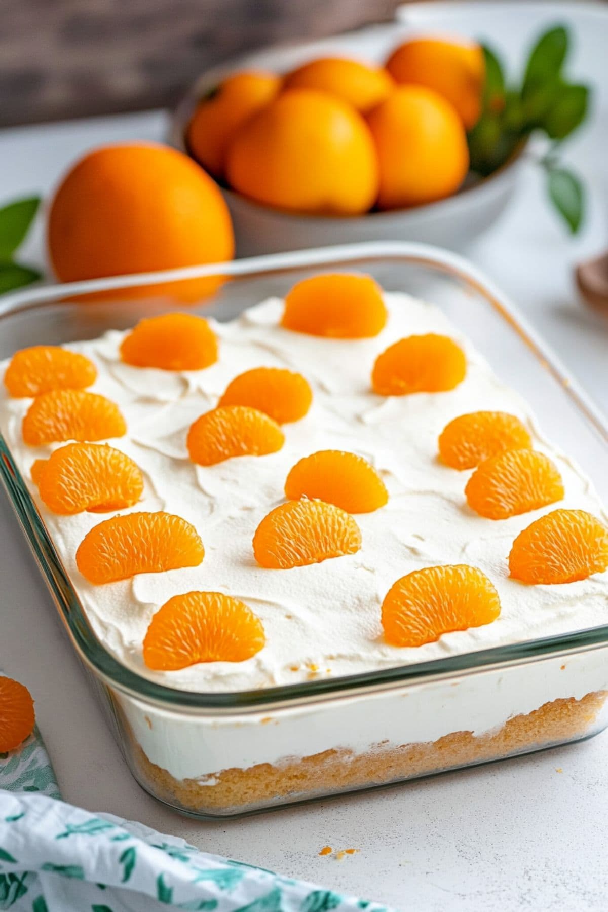 Rectangular glass baking dish with whipped cream covered cake garnished with oranges.