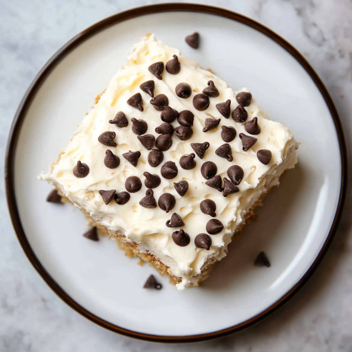 An overhead view of cannoli poke cake with vanilla frosting and topped with chocolate chips.