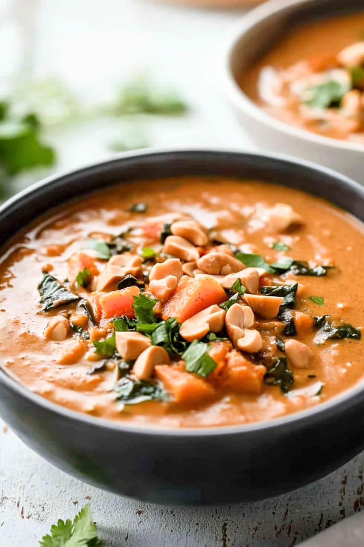 Peanut butter soup with sweet potatoes and collard greens in savory peanut butter based sauce served in a black bowl.