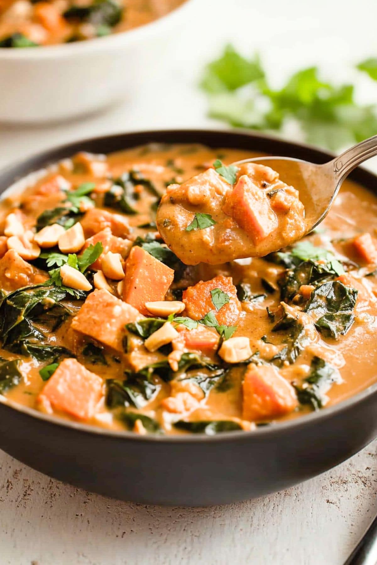 Spoon lifting a scoop of savory peanut butter soup from a serving in a black bowl.