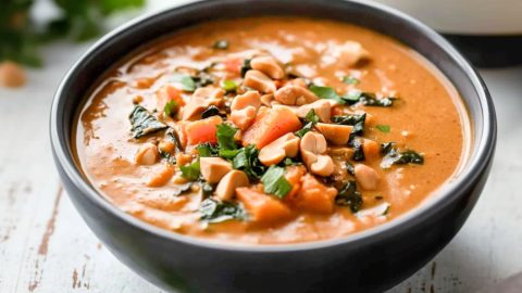 Peanut butter soup served in a black bowl garnished with chopped peanuts and cilantro.