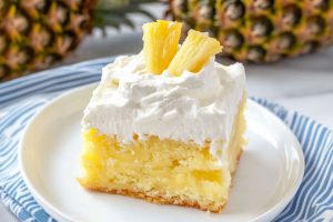 Pineapple poke cake with pineapple chunks garnish served on a white plate.