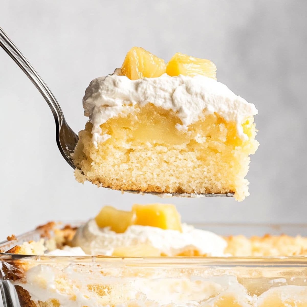 Cake ladle lifting a square slice of pineapple poke cake from the baking dish.