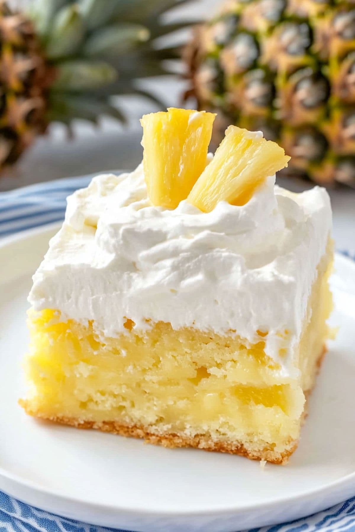 Squares slice of pineapple poke cake with pineapple chunks garnish on top of whipped cream layer.