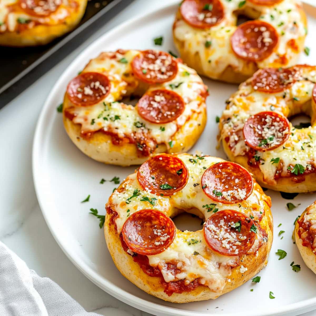 A close-up of pizza bagels with pepperoni and herbs in a white plate.