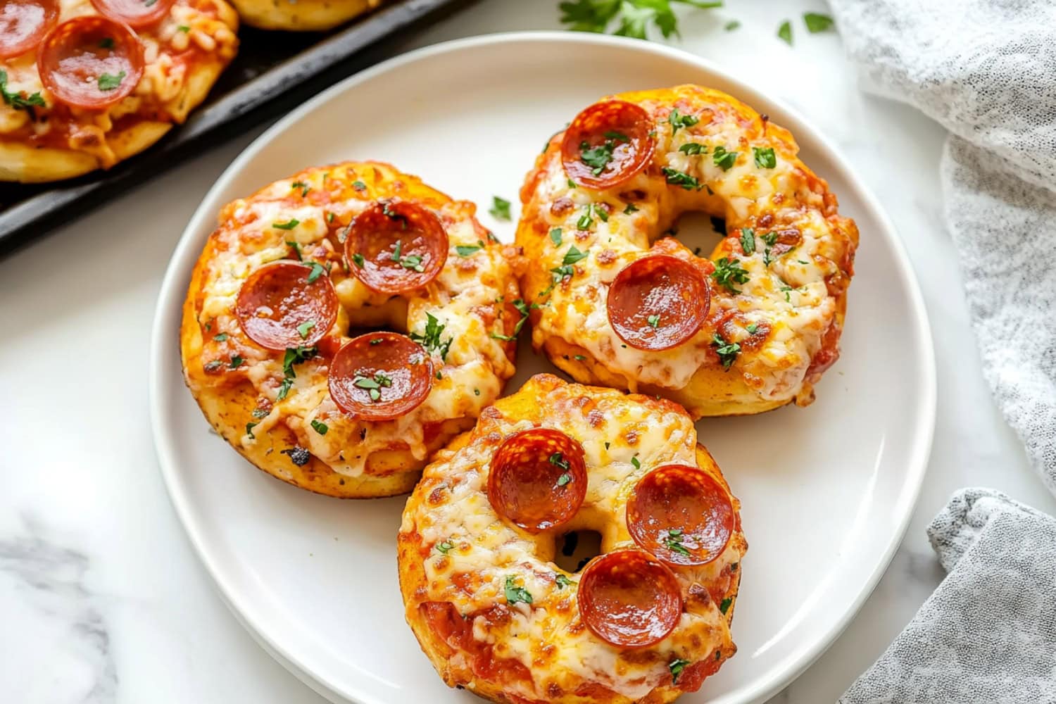 A plate of freshly baked pizza bagels with pepperoni, melted cheese and chopped parsley.