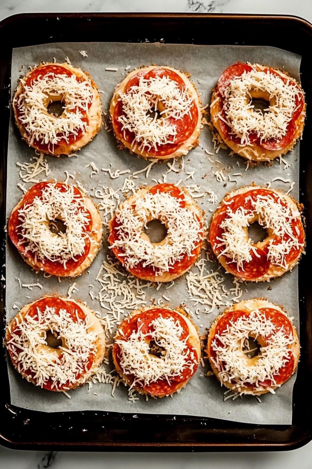 Pizza bagel with shredded cheese and pepperoni in a baking dish, overhead view.