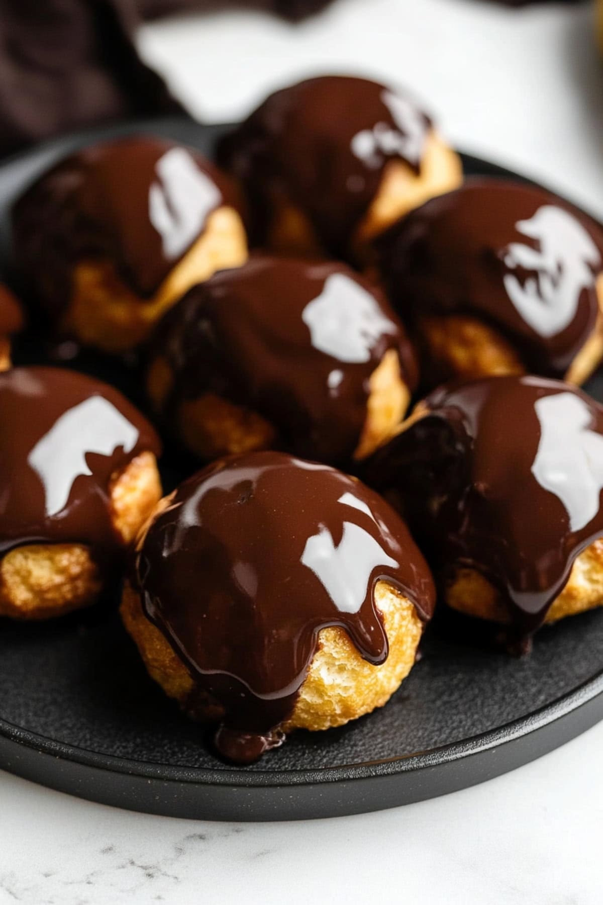 Profiteroles with Shiny Chocolate Glaze on A Black Plate