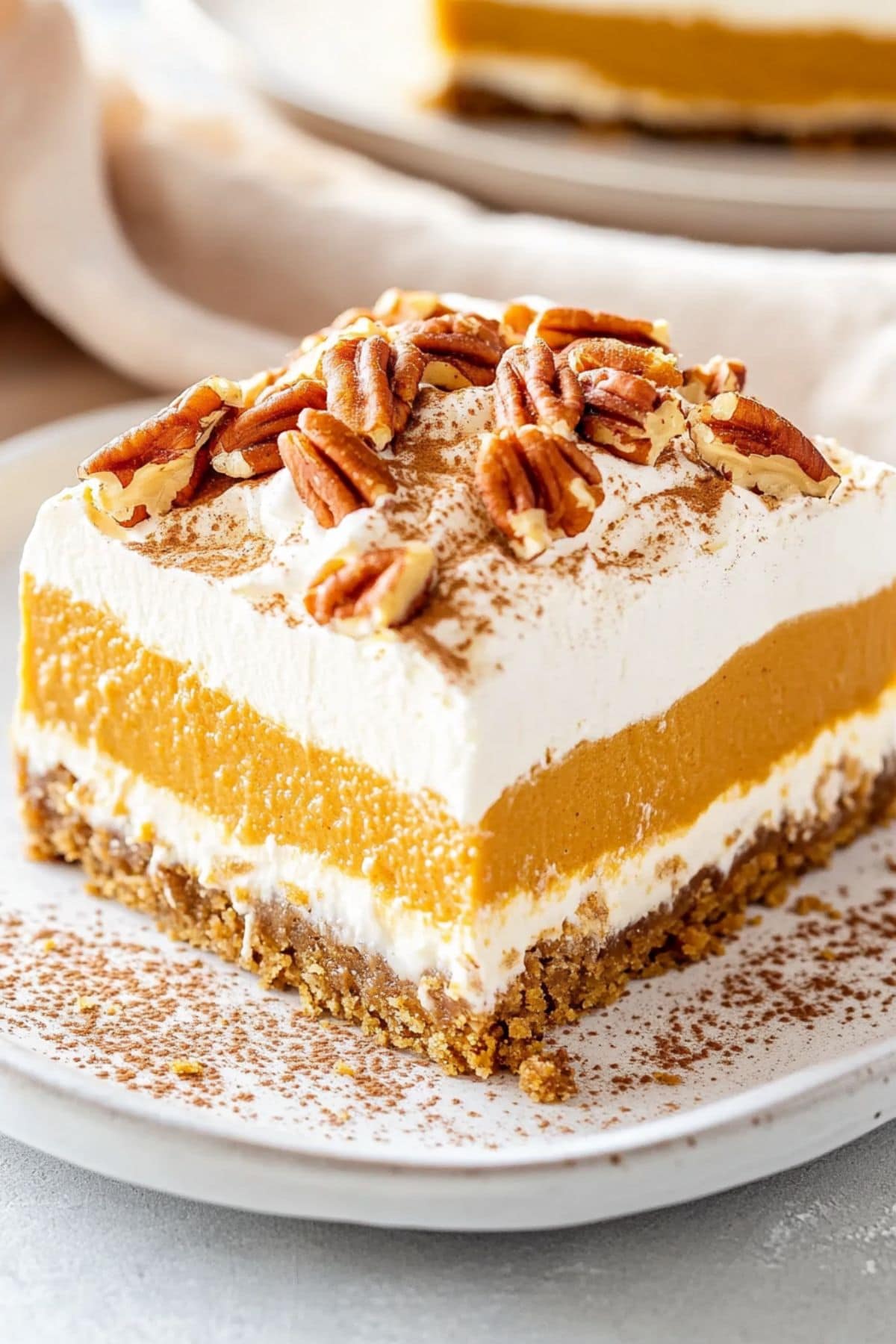 Square slice of pumpkin delight with chopped pecans and cinnamon powder on top served on a white plate.