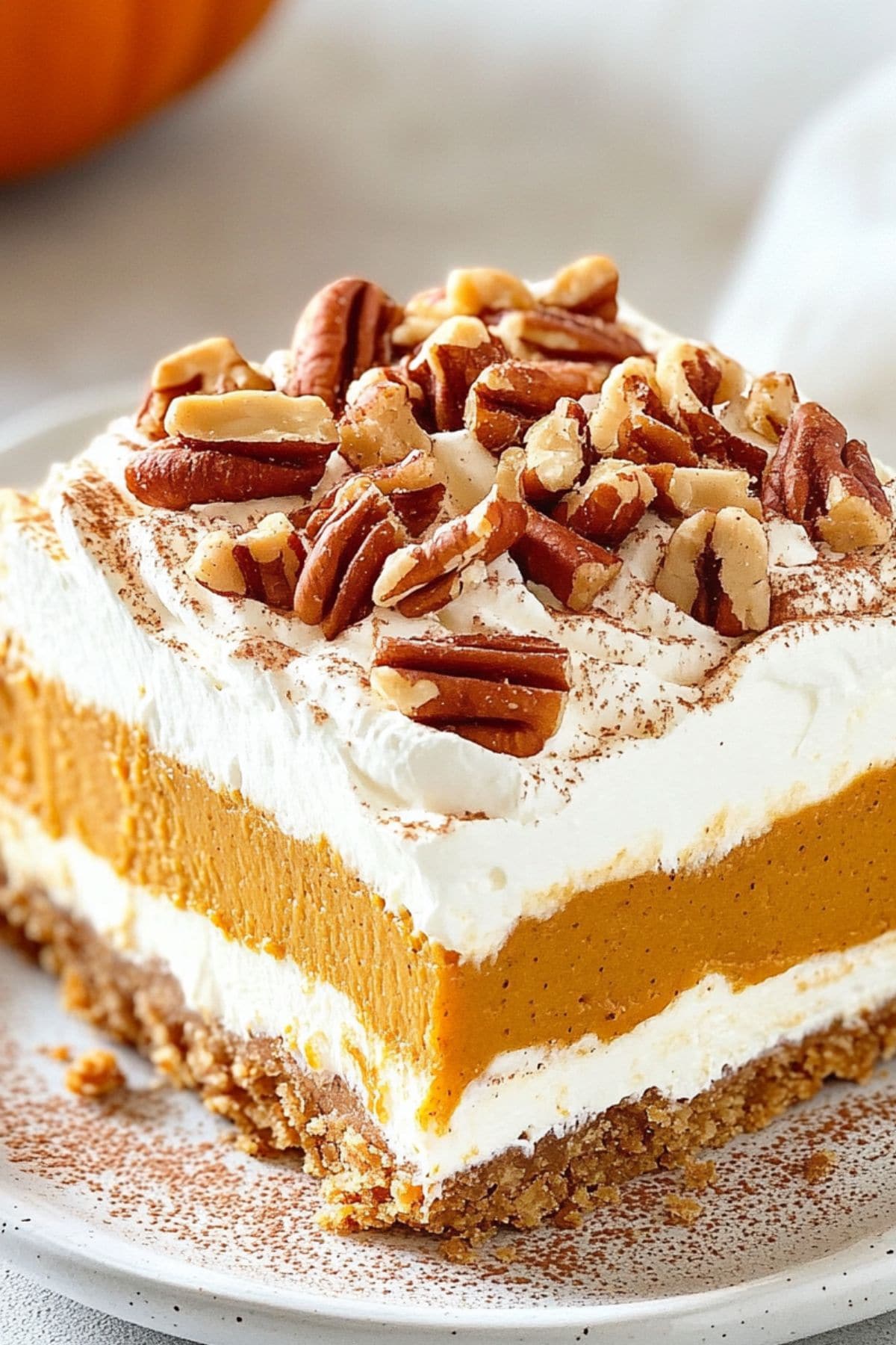 Square slice of pumpkin delight garnished with chopped pecans served in a white plate.