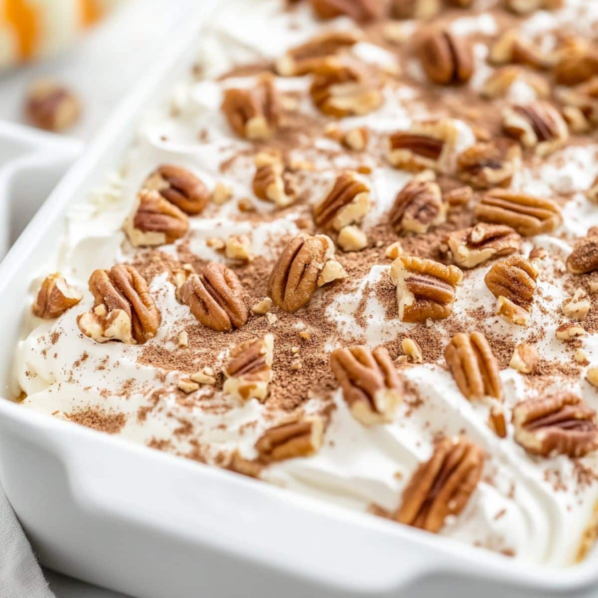 Casserole dish with pumpkin delight covered with whipped cream garnished with chopped pecans and cinnamon powder on top.