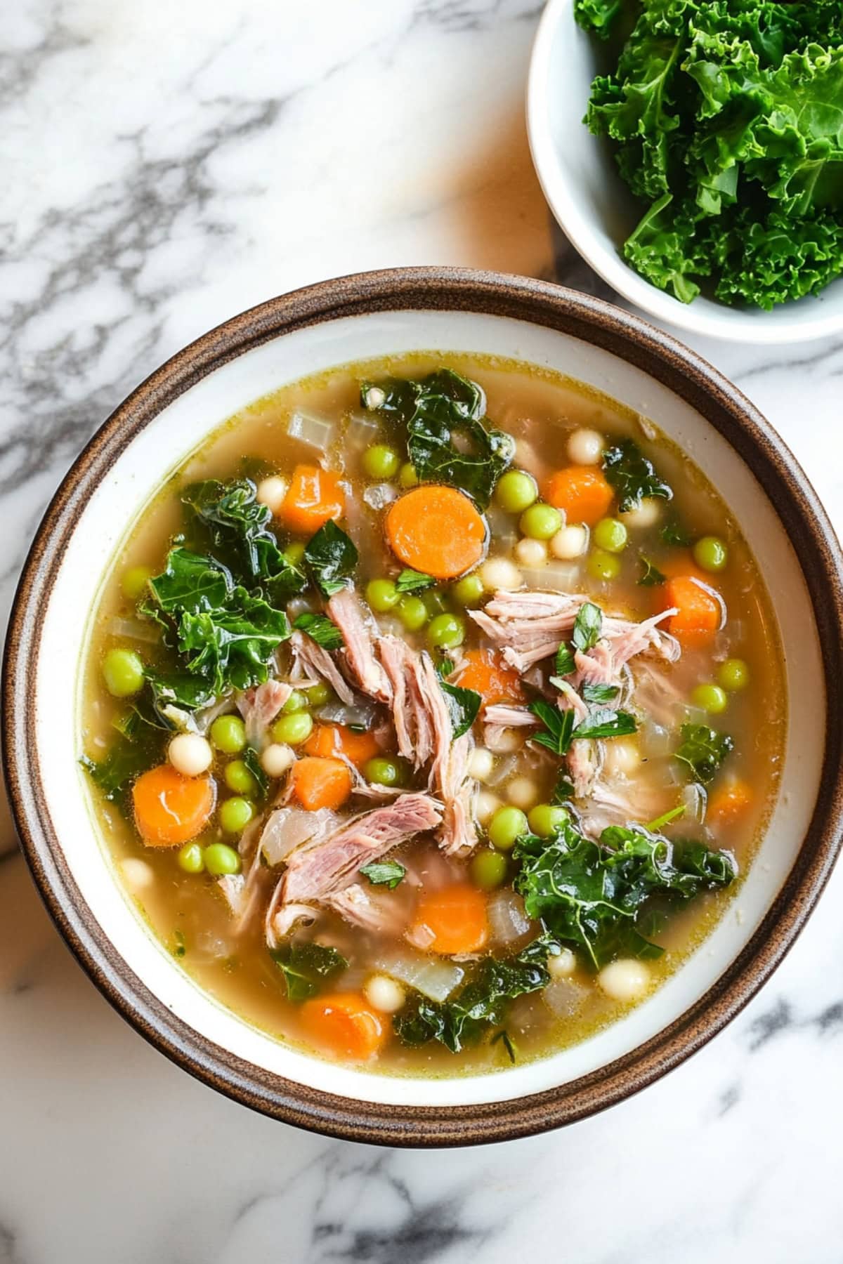 A steaming bowl of scotch broth filled with peas, kale, and carrots.