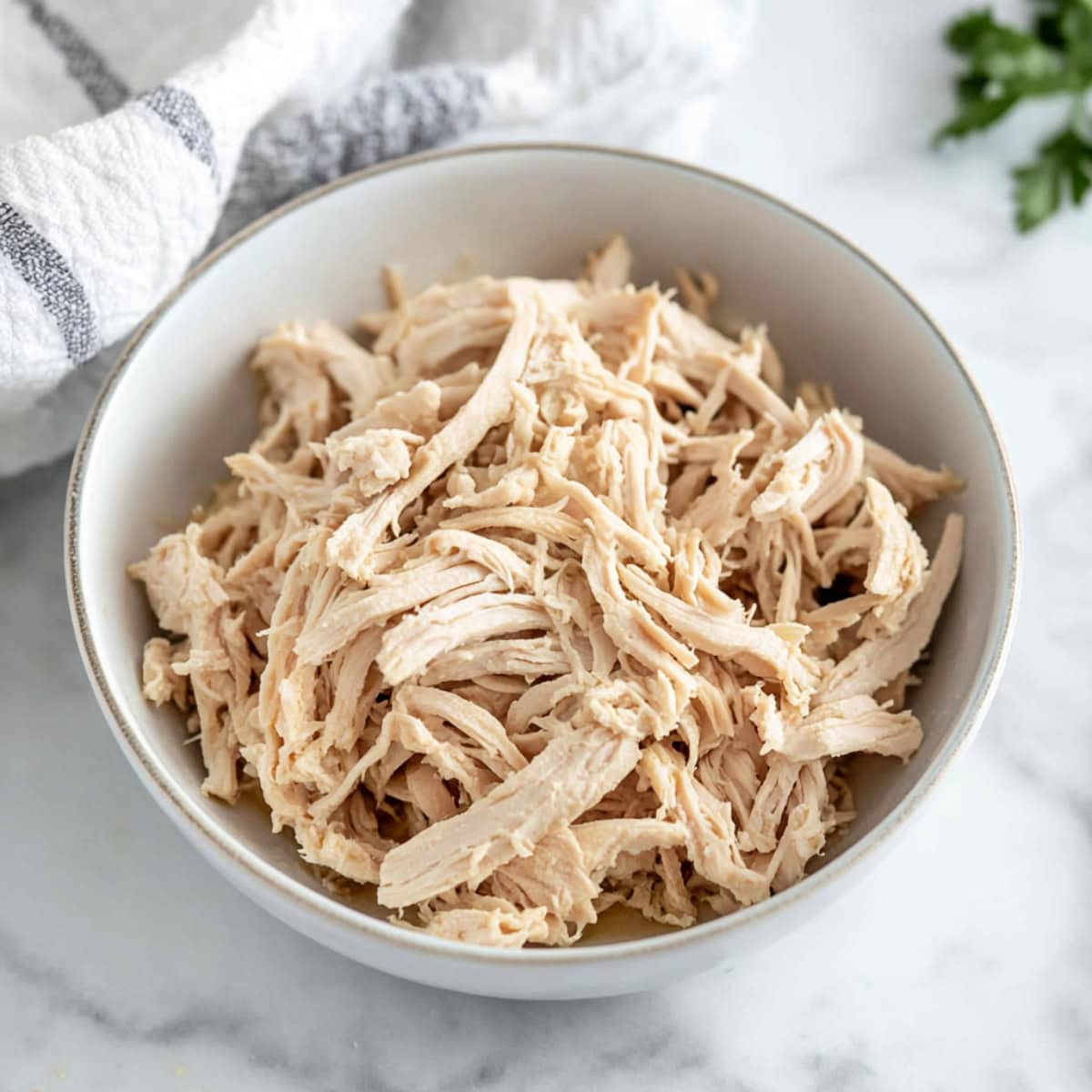 A bowl of shredded chicken on a white marble table, top view