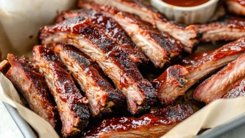 Sliced baby pork ribs in a sheet pan served with barbeque sauce.