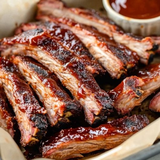 Sliced baby pork ribs in a sheet pan served with barbeque sauce.