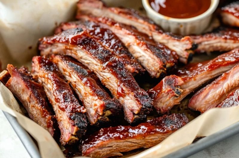 Sliced baby pork ribs in a sheet pan served with barbeque sauce.