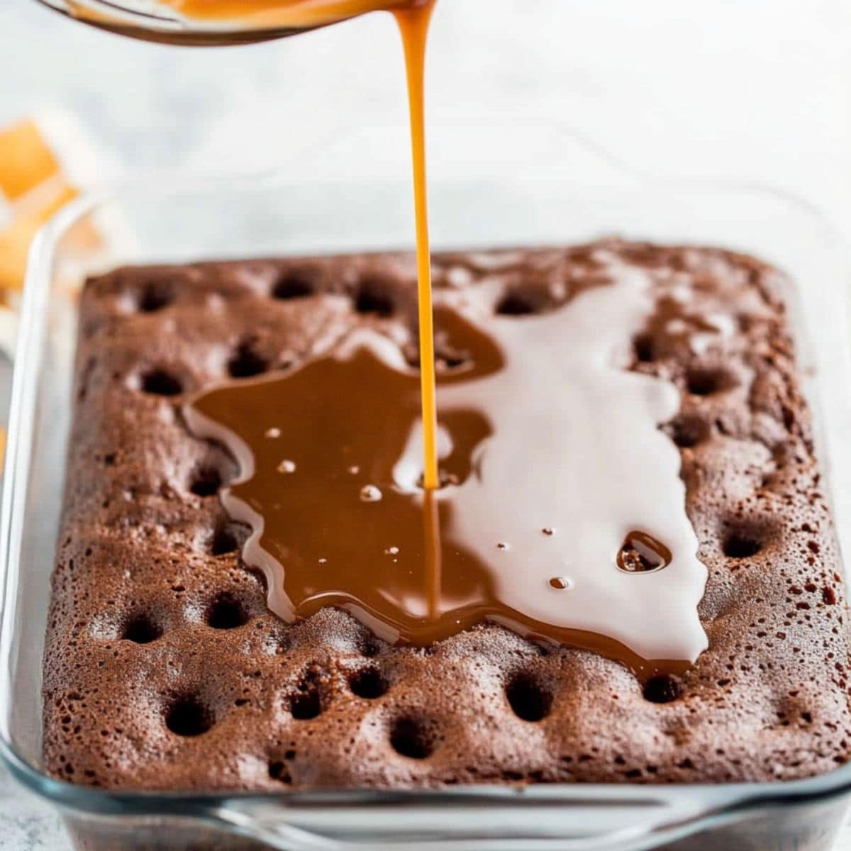 Caramel syrup poured over poked with holes chocolate cake in a baking dish.