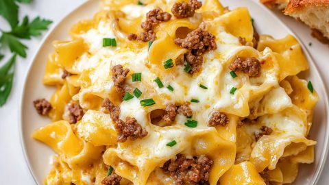 A plate of cheesy sour cream noodle bake , topped with chopped with chopped chives and a side of bread.