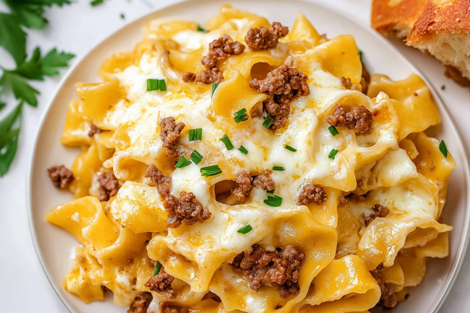 A plate of cheesy sour cream noodle bake , topped with chopped with chopped chives and a side of bread.