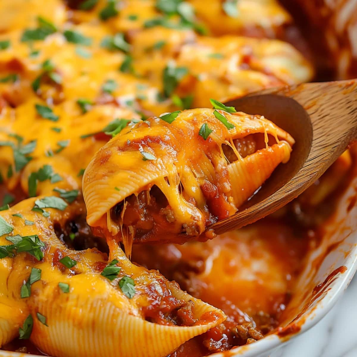 Spoon scooping out a taco stuffed shell from a baking dish