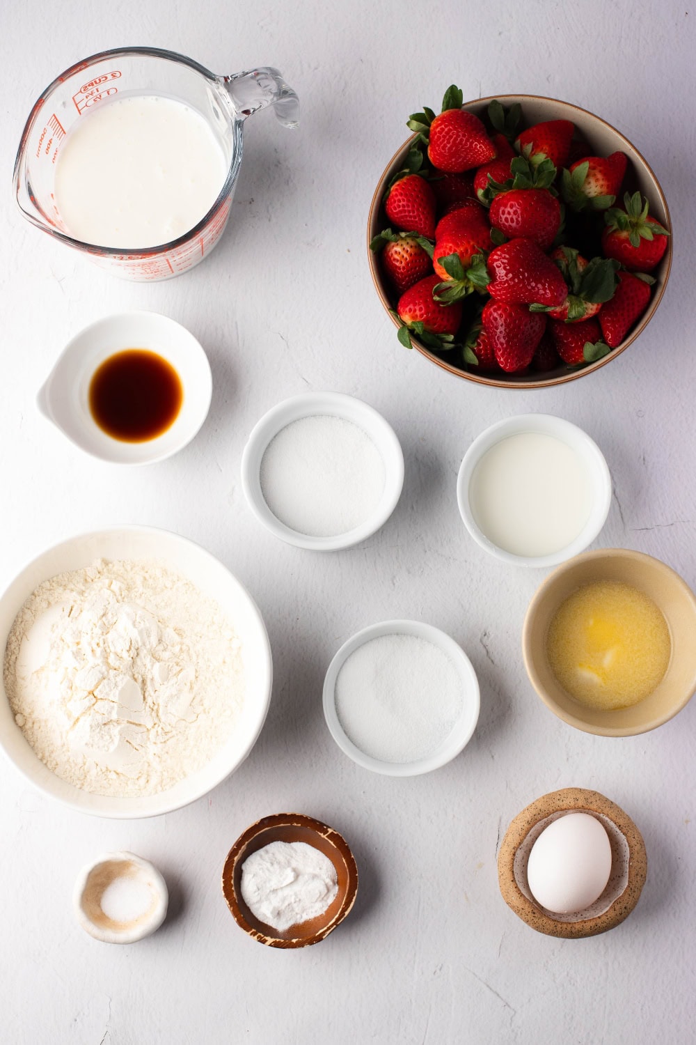 Ingredients for Strawberry Pancakes -  heavy cream, fresh strawberries, vanilla, sugar, buttermilk, flour, baking powder, melted butter, salt, and an egg. Top view