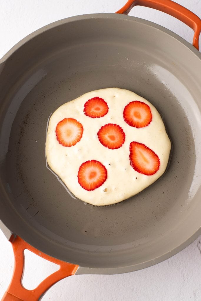A single fluffy pancake topped with fresh strawberry slices in a skillet, top view