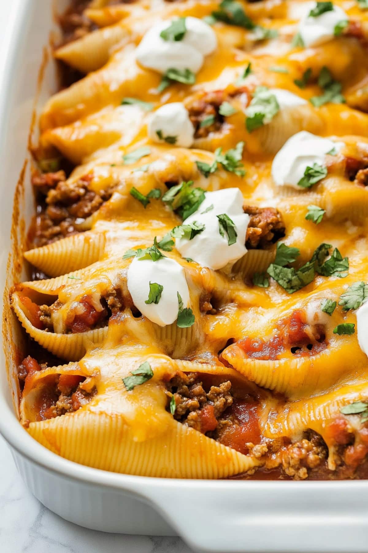 Taco stuffed shells in a white baking dish, topped with sour cream